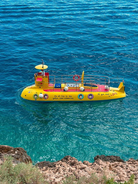 A small tourist submarine with large windows on the sea near a pine-covered peninsula