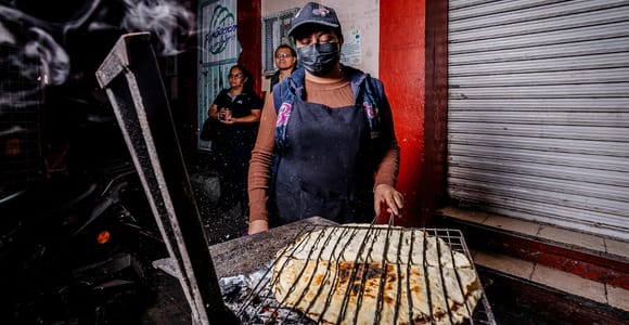 A crisp tlayuda topped with beans, cheese, greens and grilled meat at a market stall