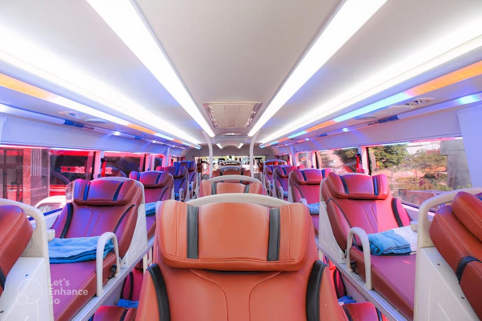 The interior of a sleeper bus with two tiers of reclined berths in orange-red leatherette under pink and blue strip lighting