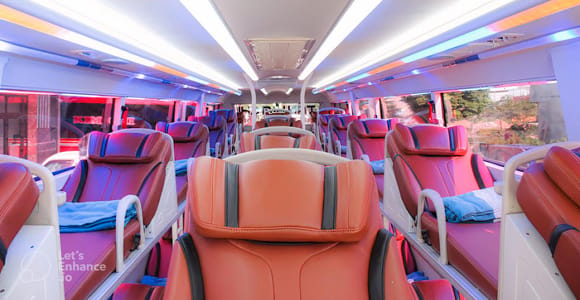 The interior of a sleeper bus with two tiers of reclined berths in orange-red leatherette under pink and blue strip lighting
