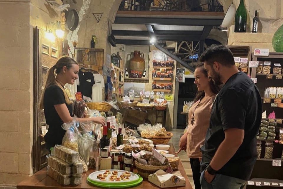 Table of local products and bottles in a stone-walled room in Matera, with a woman and two guests
