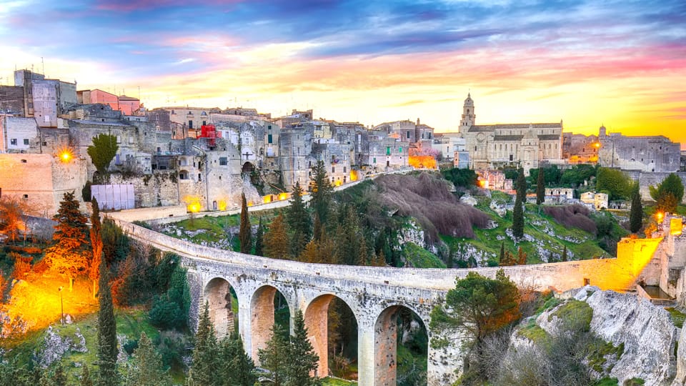 The old stone town of Gravina in Puglia at sunset, with its arched stone bridge over a wooded ravine
