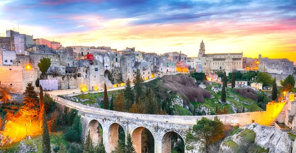 The old stone town of Gravina in Puglia at sunset, with its arched stone bridge over a wooded ravine