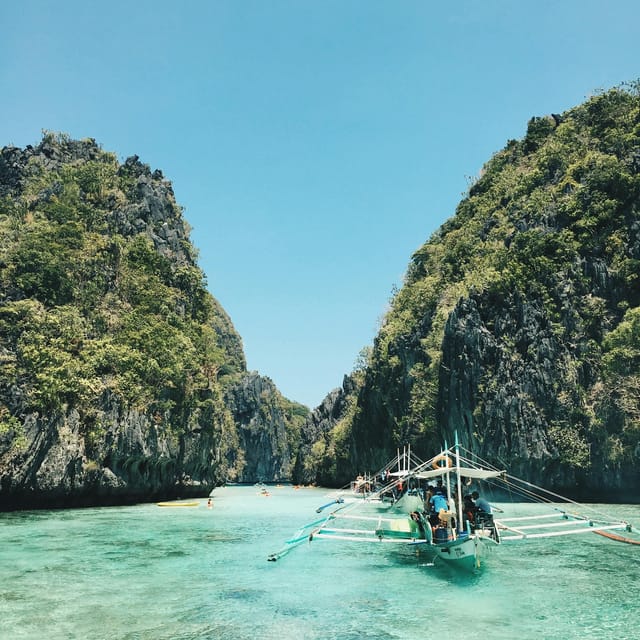 Small outrigger boat anchored off a quiet white beach in the El Nido islands