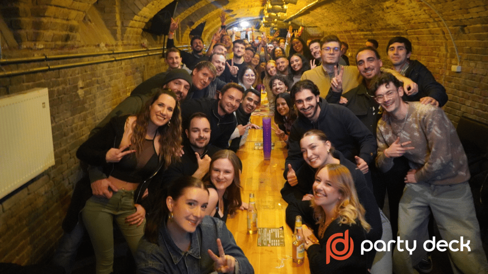 A large group of smiling guests squeezed along a long wooden table in a brick-vaulted cellar bar