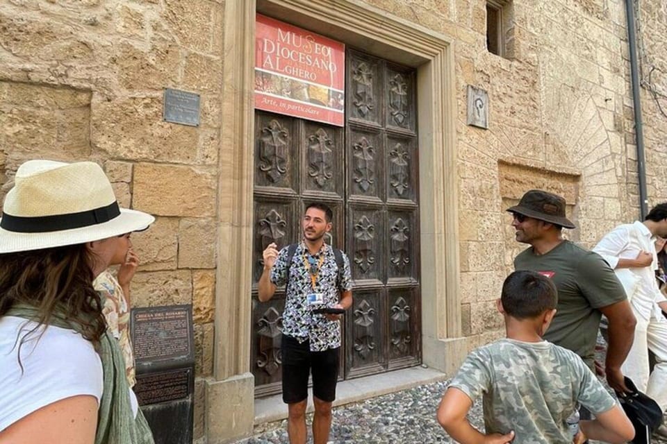 A guide in a patterned shirt talking to a small group, including a boy, in front of a carved wooden door in a sandstone wall