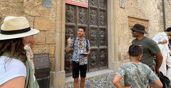 A guide in a patterned shirt talking to a small group, including a boy, in front of a carved wooden door in a sandstone wall