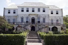 A white two-storey colonial mansion with a double stone staircase sweeping up to an arched entrance, clipped hedges in the foreground