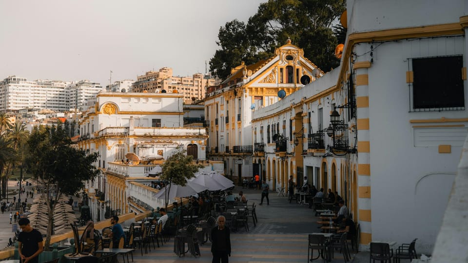 Café terraces on a square lined with cream and yellow façades in warm late light