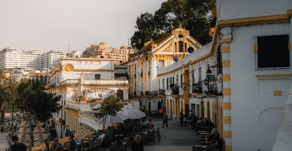 Café terraces on a square lined with cream and yellow façades in warm late light