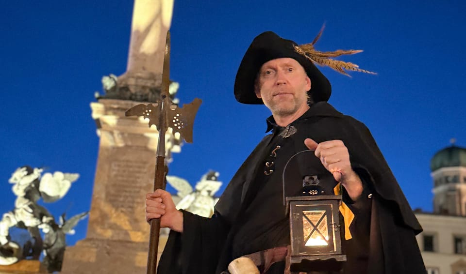Costumed night watchman with a halberd and lantern in front of the Mariensäule on Marienplatz at dusk