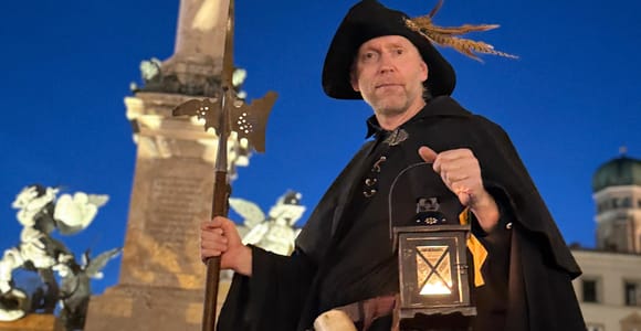 Costumed night watchman with a halberd and lantern in front of the Mariensäule on Marienplatz at dusk