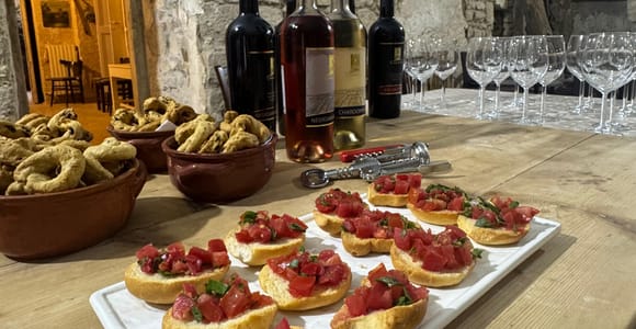 Tomato bruschetta, bowls of taralli, wine bottles and glasses on a wooden table in a stone vaulted room