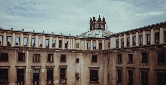 Inner courtyard of a large cream-coloured administration building with rows of windows and balconies and a domed lantern under an overcast sky