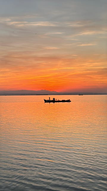 The silhouette of a small boat on the wide Albufera lagoon under an orange evening sky