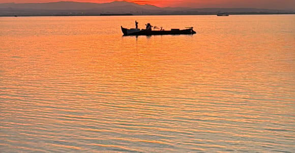 The silhouette of a small boat on the wide Albufera lagoon under an orange evening sky