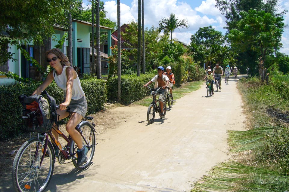 Cyclists following a narrow path between bright green rice fields near Hoi An