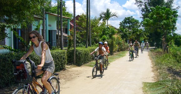 Cyclists following a narrow path between bright green rice fields near Hoi An