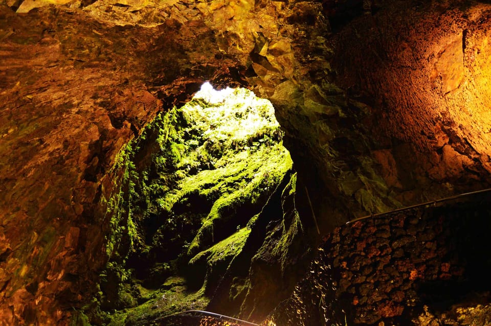 Visitors with torches walking down into a dark volcanic cavity lined with rough basalt