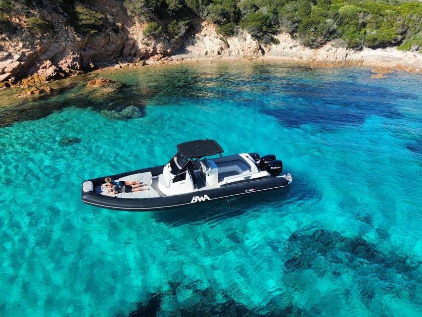 Un grand semi-rigide noir et blanc au mouillage dans une eau limpide et turquoise devant une côte rocheuse boisée