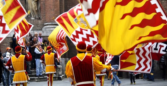 Contrada flags hanging above a narrow brick street in Siena