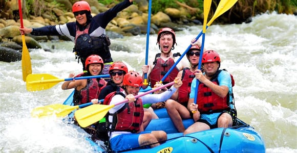 A rafting team paddling through white water between forested riverbanks