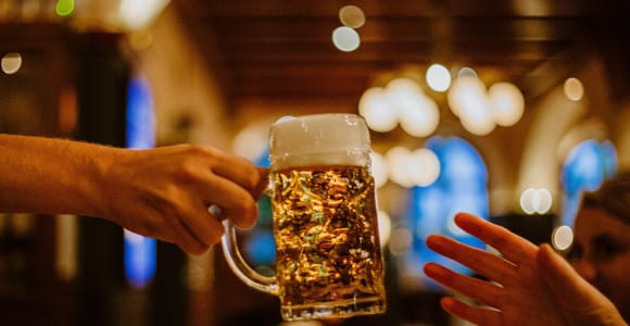 A hand passing a full glass beer mug across a table in a warmly lit beer hall