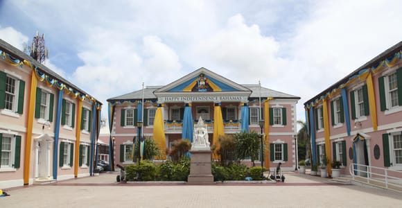 Parliament Square in Nassau: pink colonial buildings with green shutters draped in yellow and blue bunting around a white marble statue of Queen Victoria on a paved forecourt