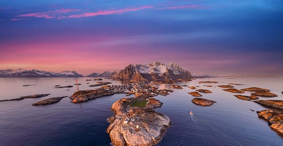 Red fishing cabins clustered around a sheltered Lofoten harbour beneath steep rock walls