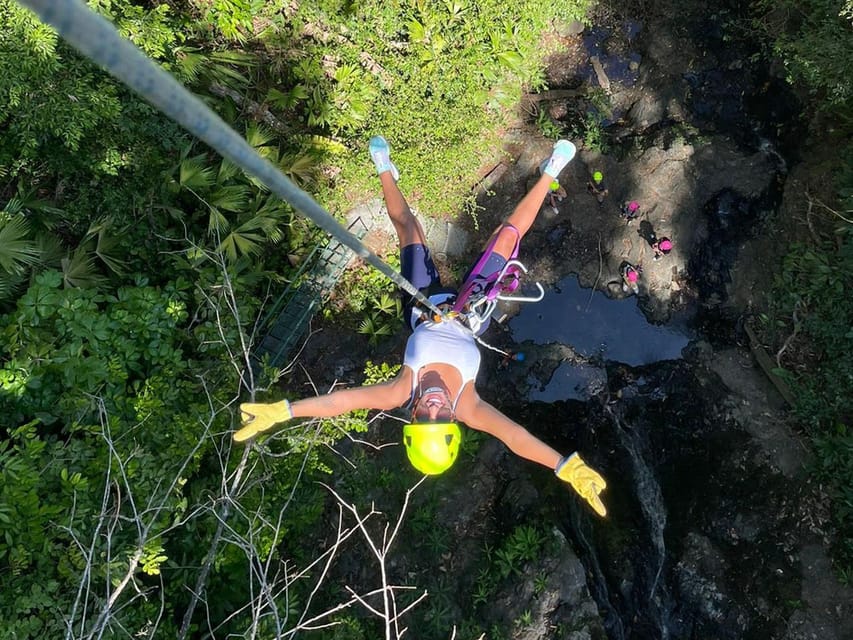 A traveller wearing a helmet gliding on a zipline above dense green forest