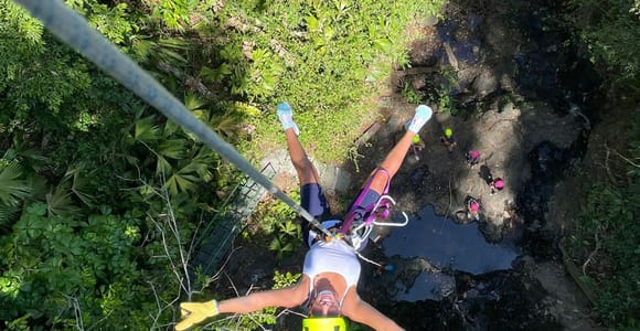 A traveller wearing a helmet gliding on a zipline above dense green forest