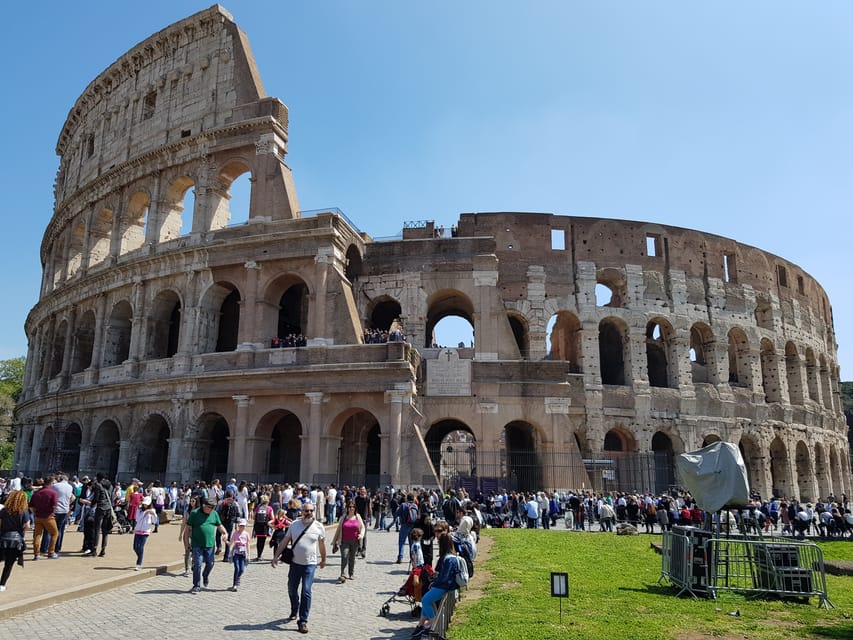 Guide with a radio headset addressing a small group in the shade of the Colosseum's outer arcade