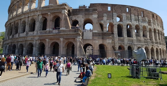 Guide with a radio headset addressing a small group in the shade of the Colosseum's outer arcade