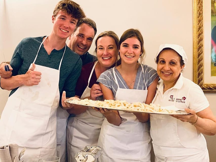 Five smiling people in aprons holding a tray of freshly cut pasta indoors