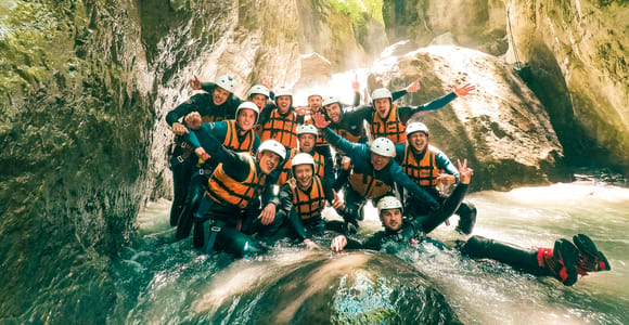 A canyoning group in wetsuits and helmets standing in a narrow rock gorge with water running through it