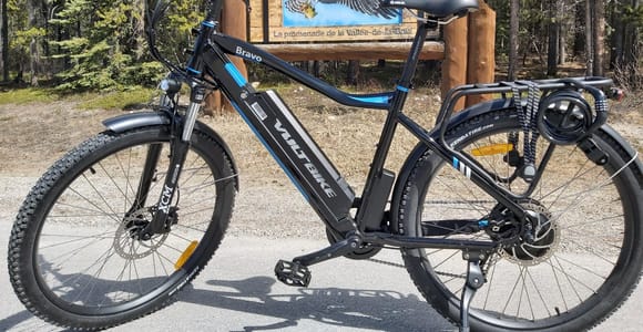 A black electric mountain bike beside a Bow Valley Parkway sign in a pine forest