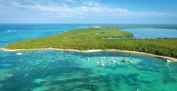 White catamaran under sail on flat turquoise water, passengers sitting along the trampoline deck at the bow