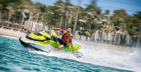 Ein Fahrer lenkt einen Jetski nahe einer palmenbestandenen Küste