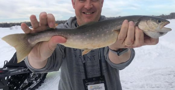 An angler lowering a line through an ice hole inside a heated wooden fishing cabin