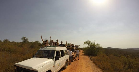 A white off-road vehicle on a red dirt track through low scrub in the Algarve hinterland, sun high above the ridge
