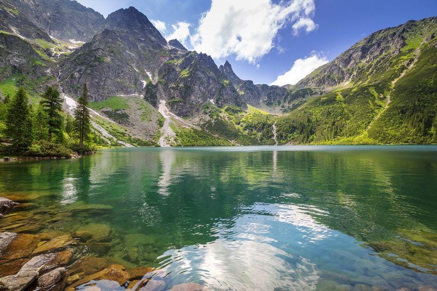 Mountain lake with green water beneath steep rocky peaks, pine trees on the shore