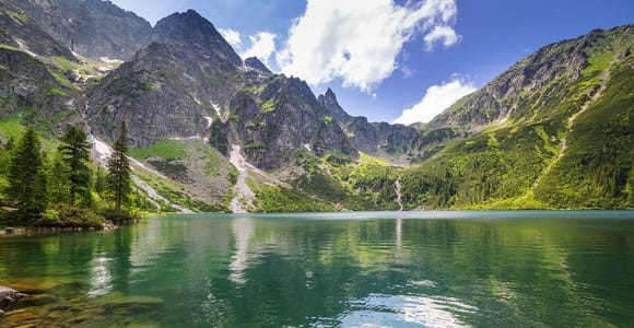 Mountain lake with green water beneath steep rocky peaks, pine trees on the shore
