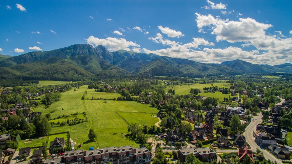 Aerial view of Zakopane with houses and meadows in front of a forested mountain massif