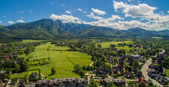 Aerial view of Zakopane with houses and meadows in front of a forested mountain massif