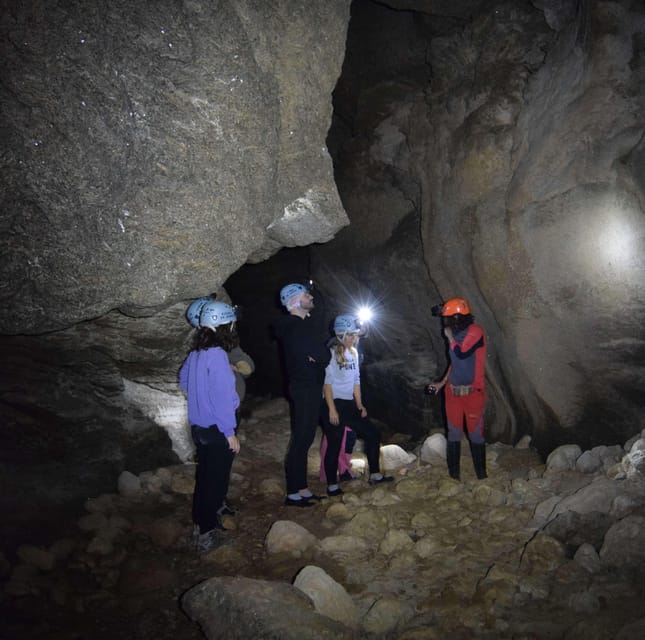Four people in helmets and head torches stand in a dark cave passage