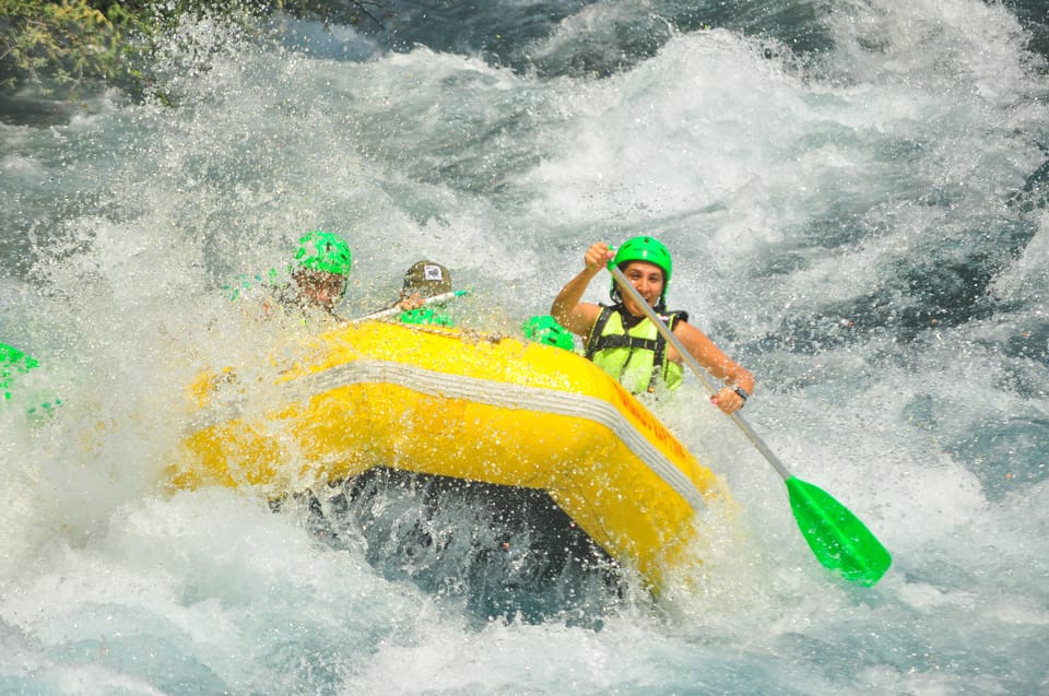 Yellow raft with helmeted paddlers plunging through white water, spray covering the bow