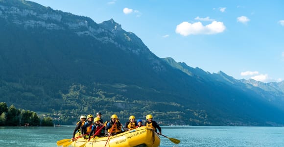 A group in helmets and life jackets paddling a yellow raft on a turquoise lake below steep mountains