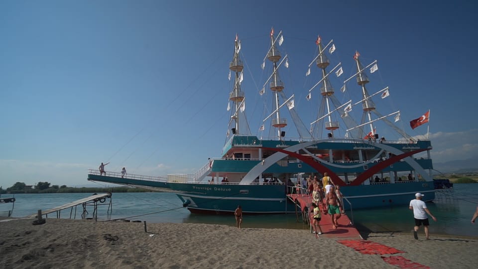 A large excursion boat with several masts at the shore as guests board