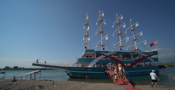 A large excursion boat with several masts at the shore as guests board