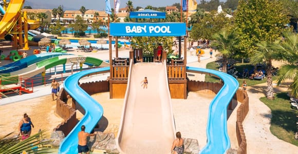 Colourful family water slides and shallow pools surrounded by trees at Aqualand Corfu
